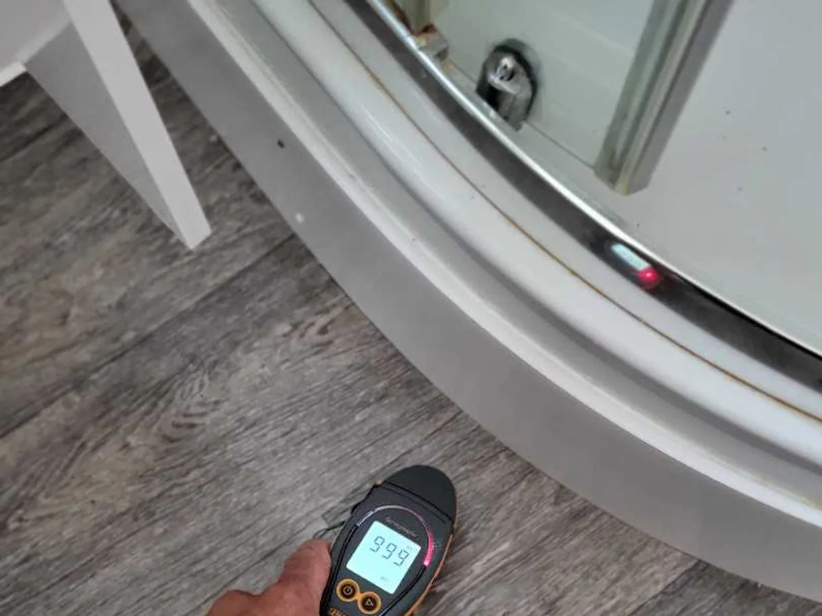 Surveymaster moisture meter reading 999 WET held near a shower enclosure during an internal mains leak detection at a property in WF8