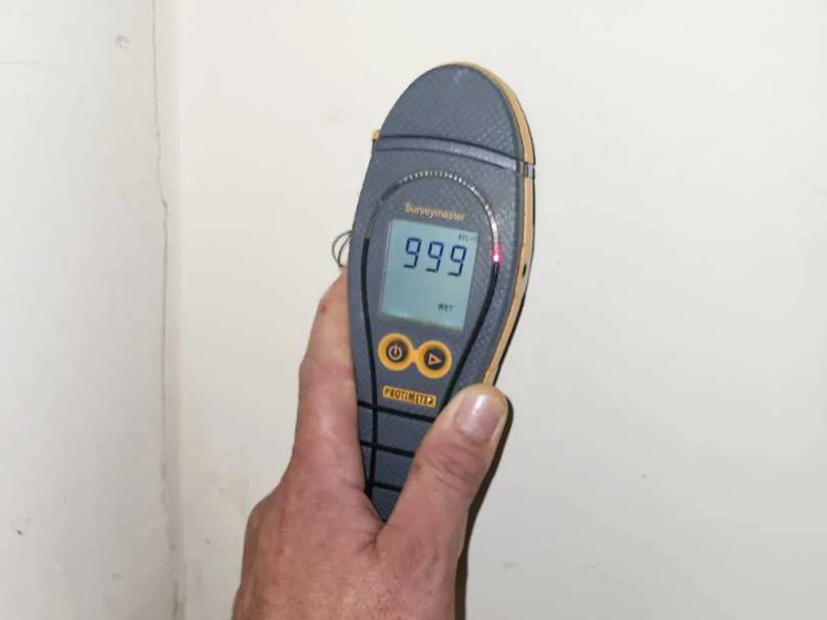 Surveymaster moisture meter reading 999 WET held against a wall during an internal mains leak detection survey at a property in WF8