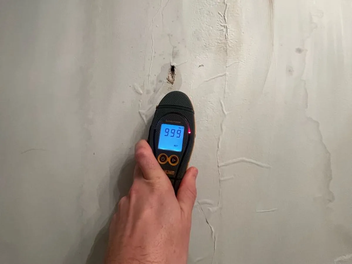Surveymaster moisture meter reading 999 WET held against a damaged wall during a hot water leak detection at a property in Uxbridge