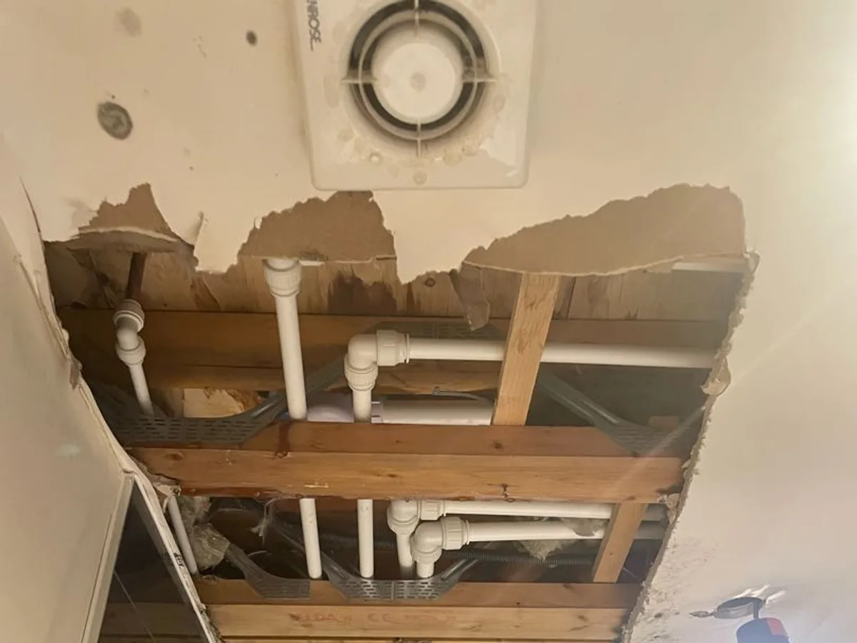 Collapsed ceiling exposing waste pipework inside a floor void during a hot water leak detection survey at a property in Uxbridge