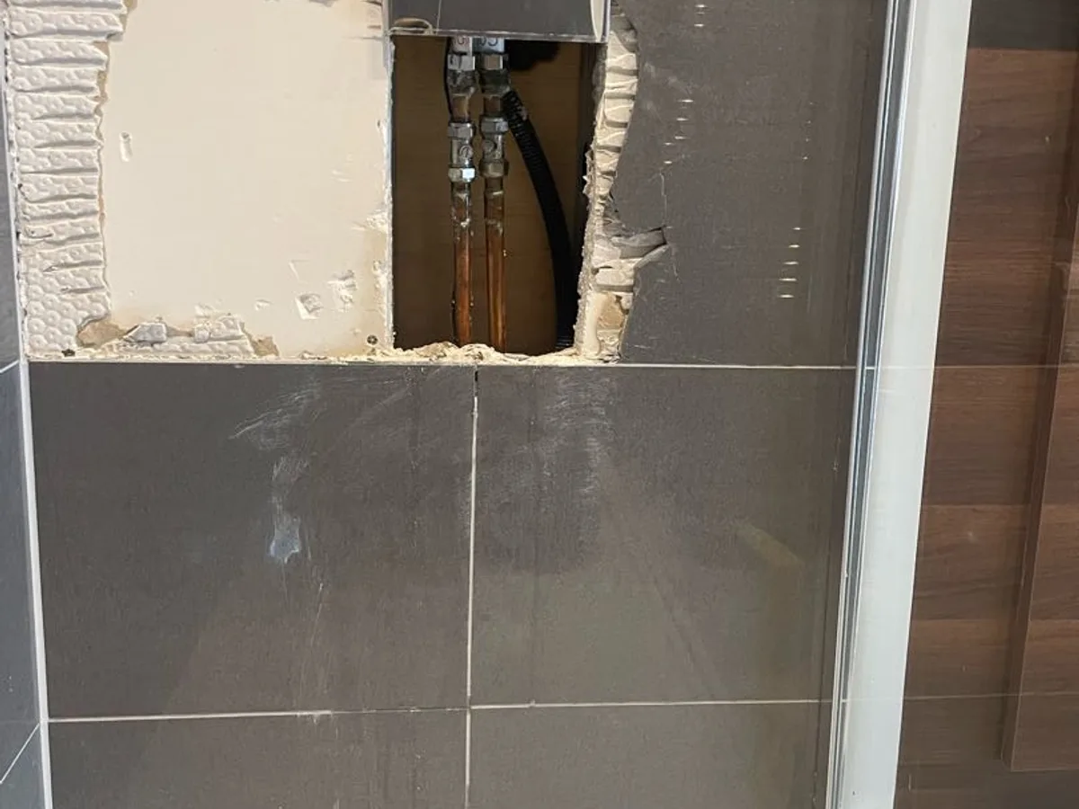 Hole cut through tiled shower wall exposing copper hot water pipes during a hot water leak detection survey at a property in Uxbridge