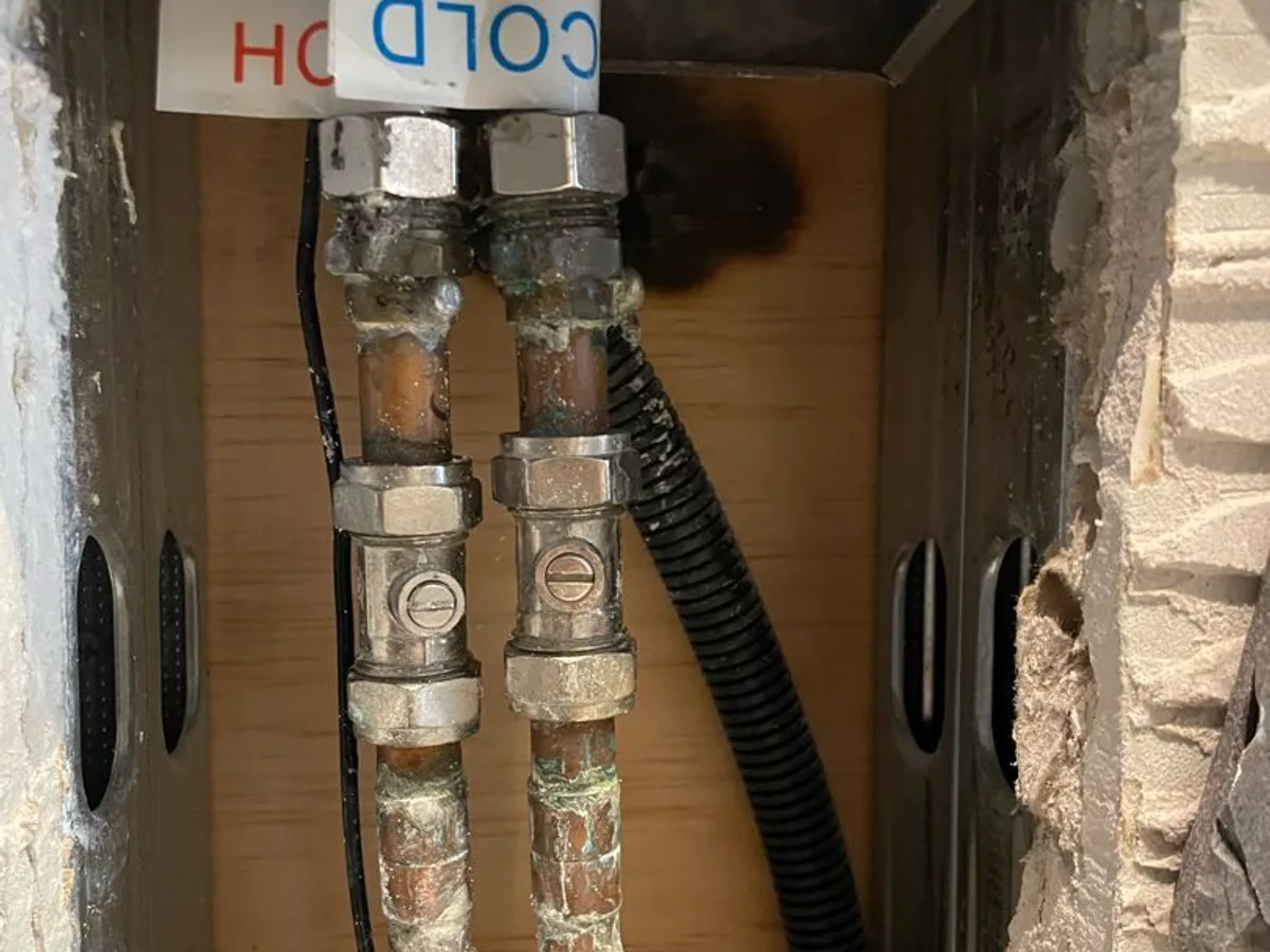Corroded hot and cold water pipes with isolation valves inside a wall cavity during a hot water leak detection survey at a property in Uxbridge