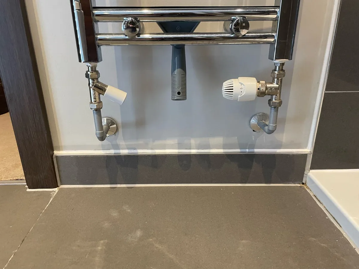 Thermostatic radiator valve and angled pipe connections at the base of a chrome towel rail during a hot water leak detection survey at a property in Uxbridge