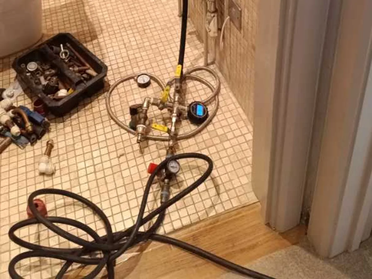 Pressure testing gauges and hoses connected to valves on a tiled floor during a central heating leak detection survey at a property in BA3