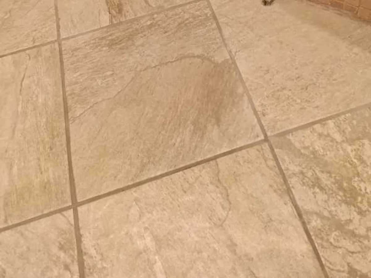 Damp wet patch on stone-effect floor tiles indicating a central heating leak at a property in BA3