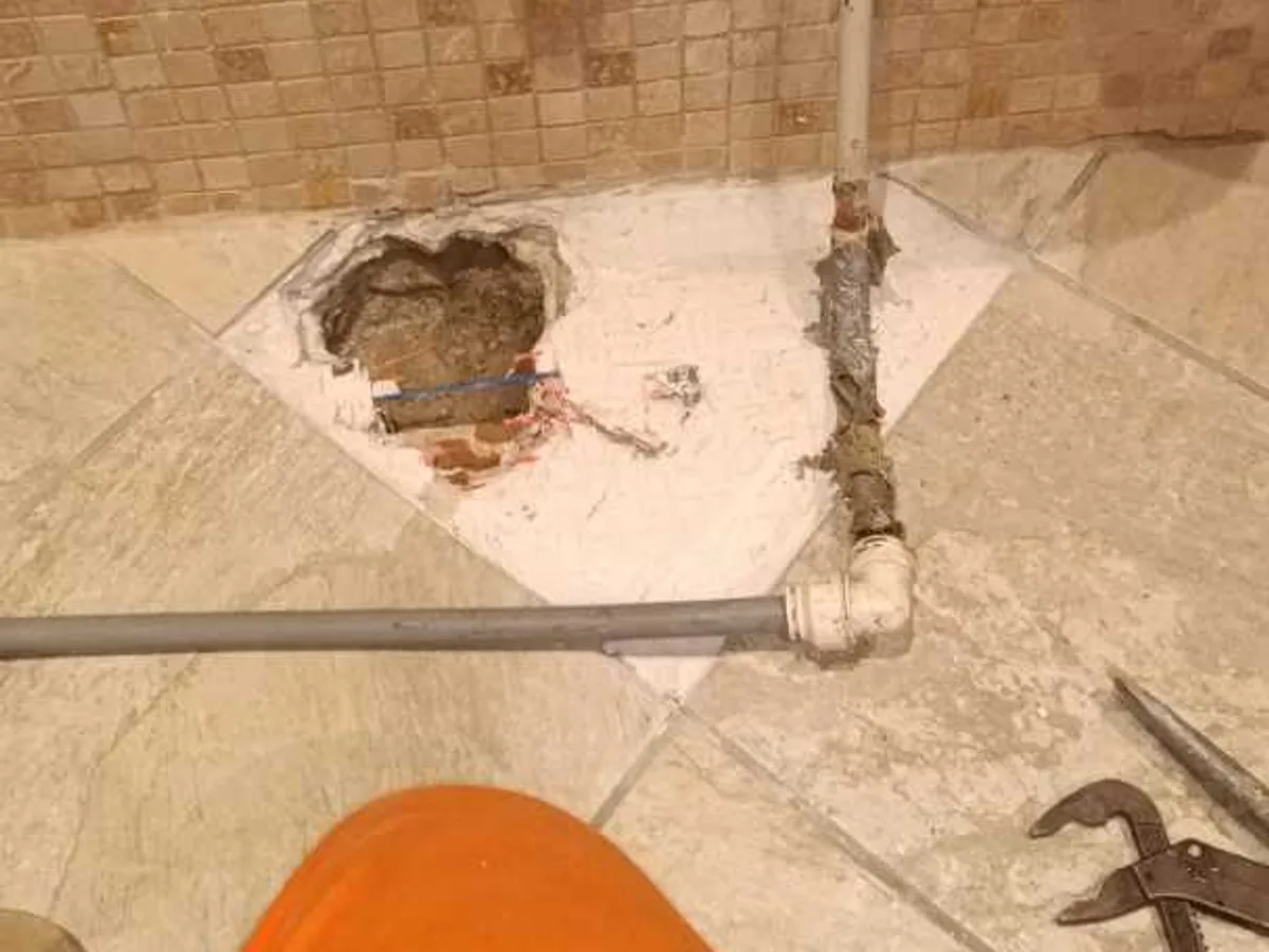 Broken floor tiles and exposed pipework with elbow joint during a central heating leak investigation at a property in BA3