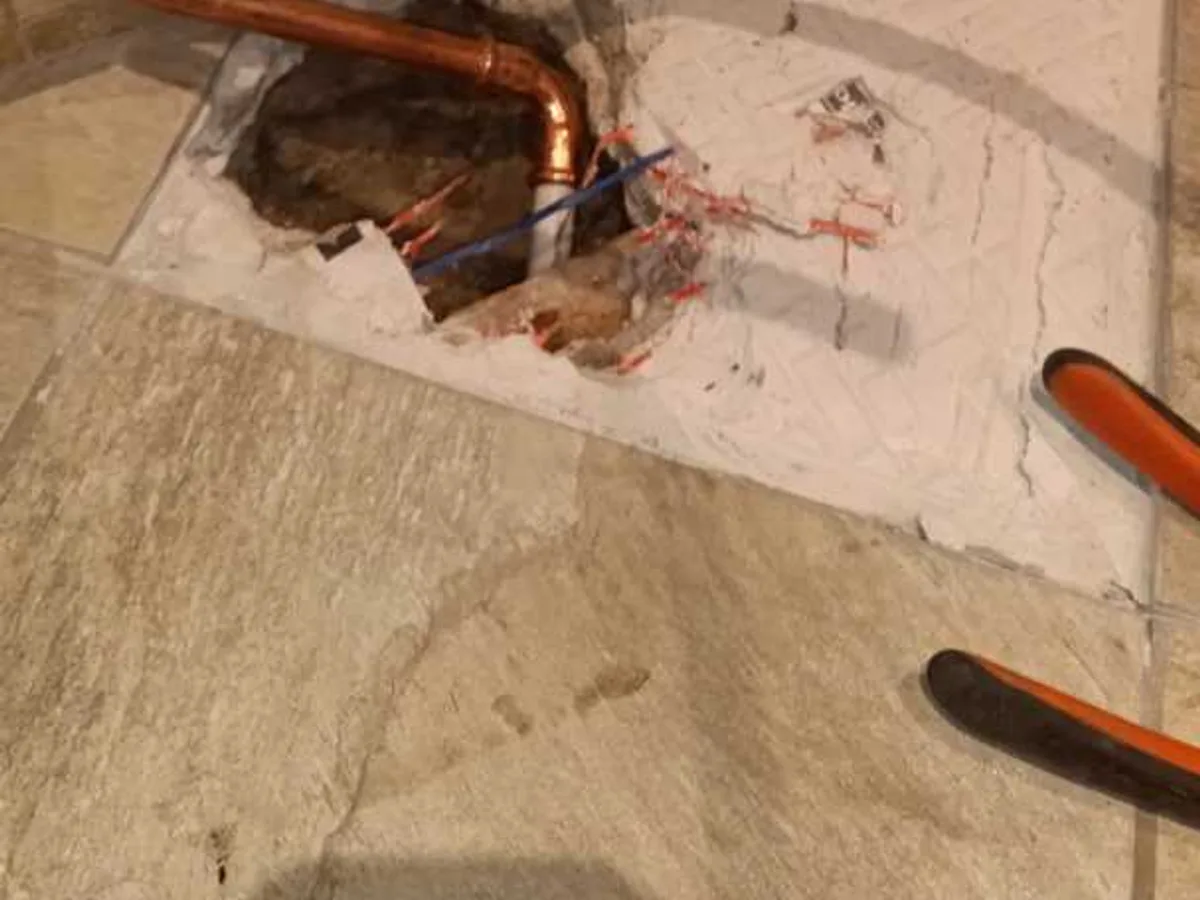Copper pipes exposed through broken floor tiles during a central heating leak detection survey at a property in BA3