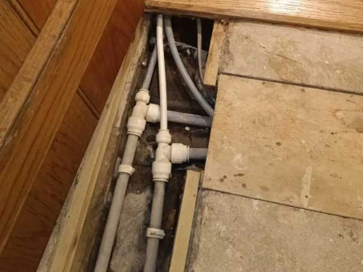 Exposed plastic push-fit pipe fittings inside an underfloor void during a central heating leak detection survey at a property in BA3