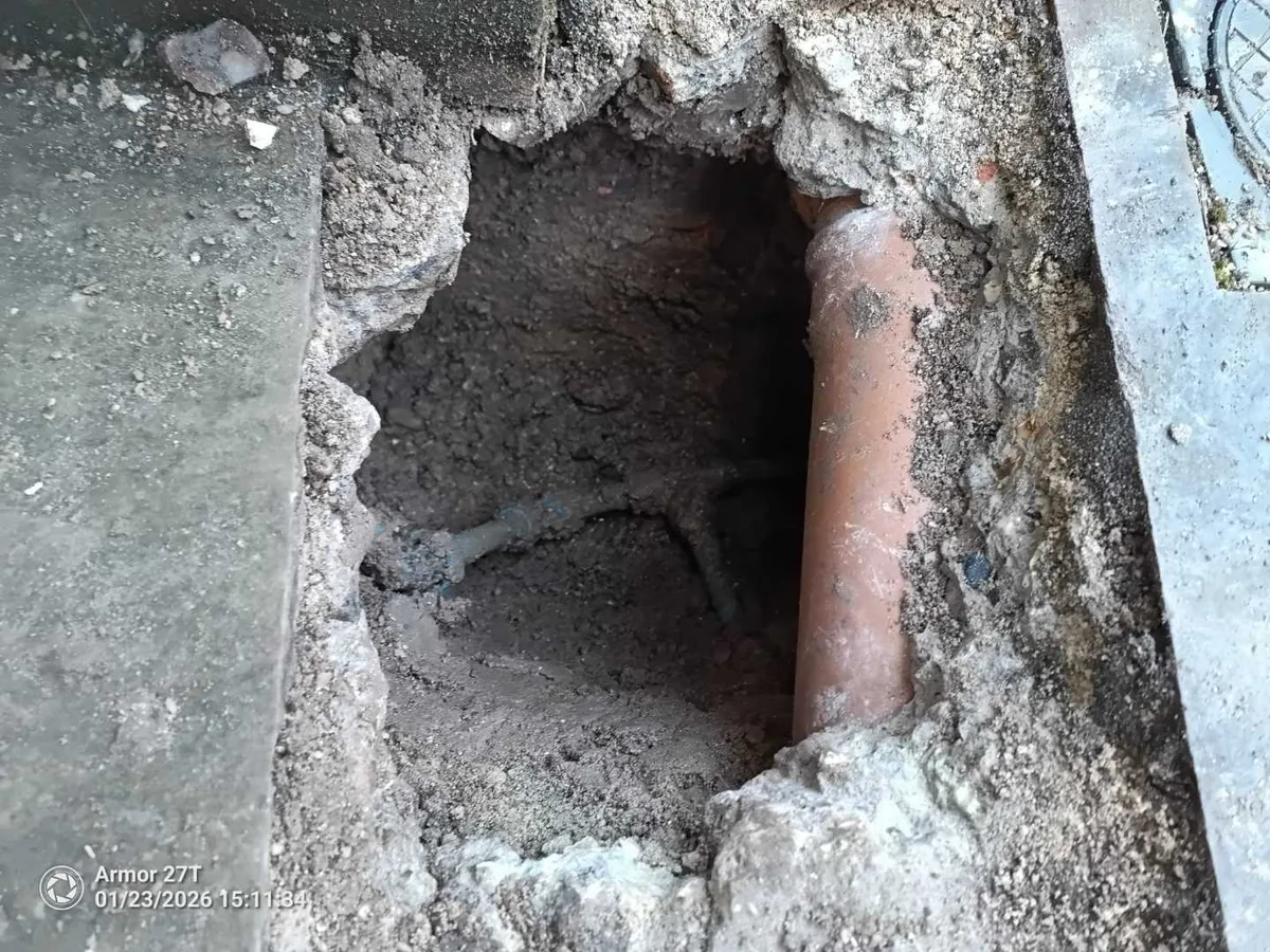 Excavated hole exposing a clay drain pipe buried in soil during an underground mains leak detection survey at a property in SN8