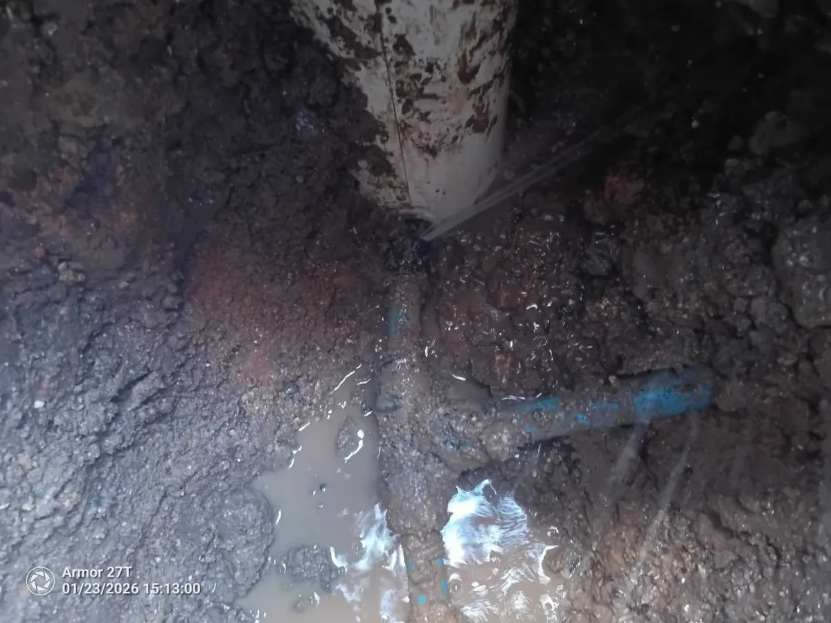 Excavated trench with water pooling around a blue water mains pipe during an underground leak detection survey at a property in SN8