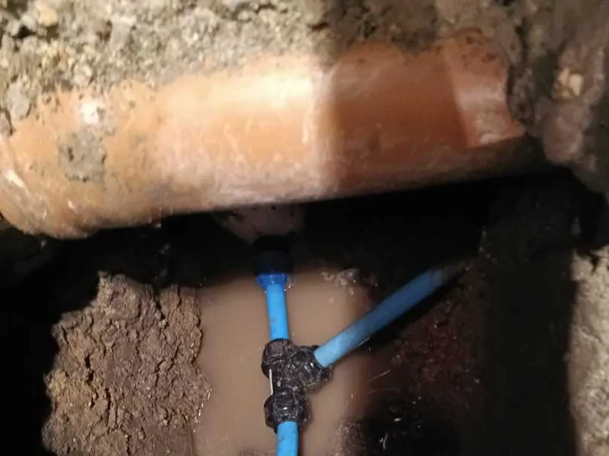Blue mains water pipe with push-fit connector exposed during underground leak detection excavation at a property in SN8