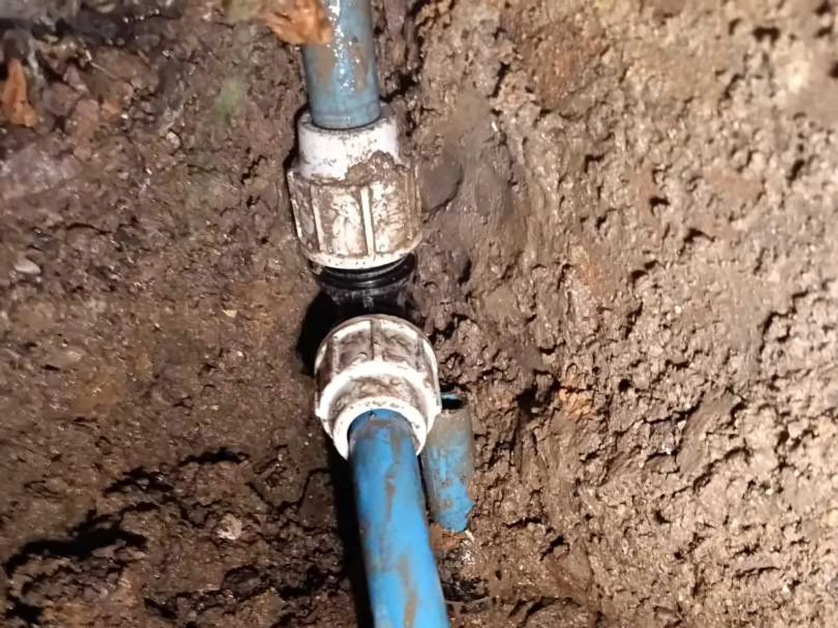 Compression fittings joining blue polyethylene water mains pipe exposed during underground leak detection at a property in SN8