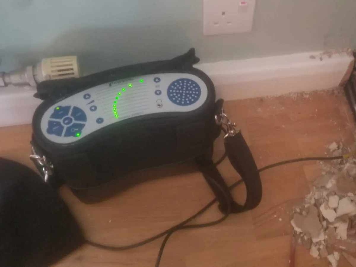 tracer gas detector beside lifted skirting board in living room during leak detection survey