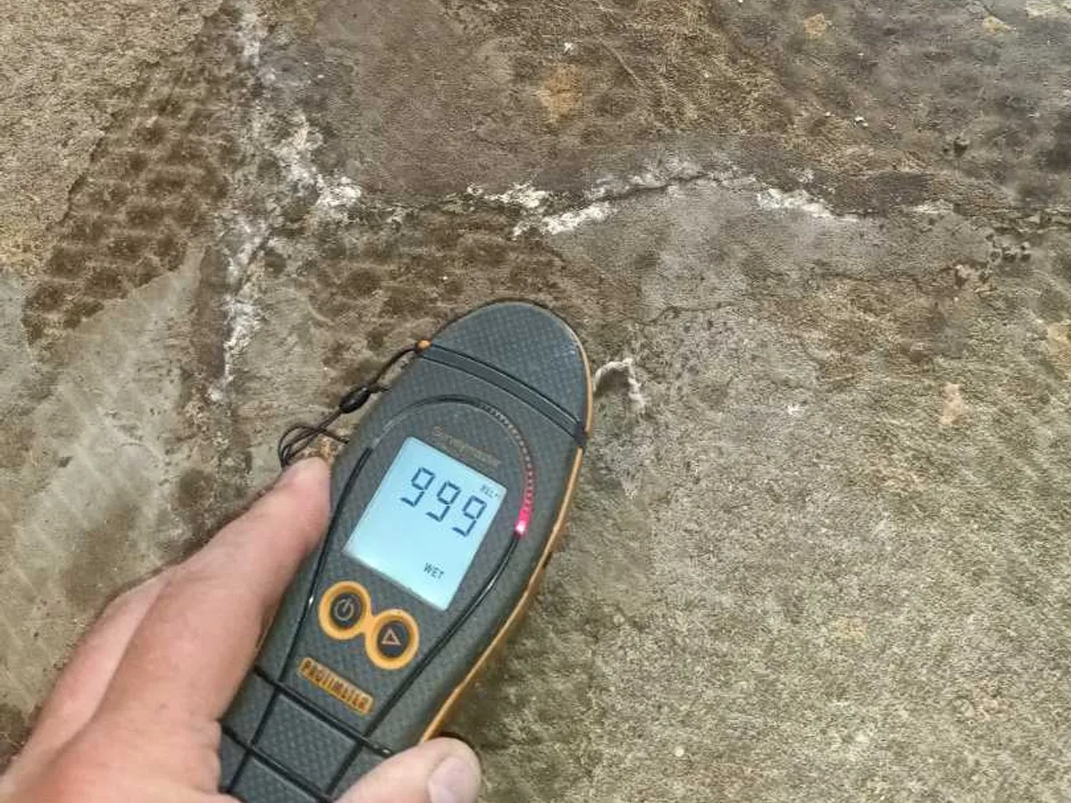damp meter reading 999 on saturated hallway concrete floor during leak detection