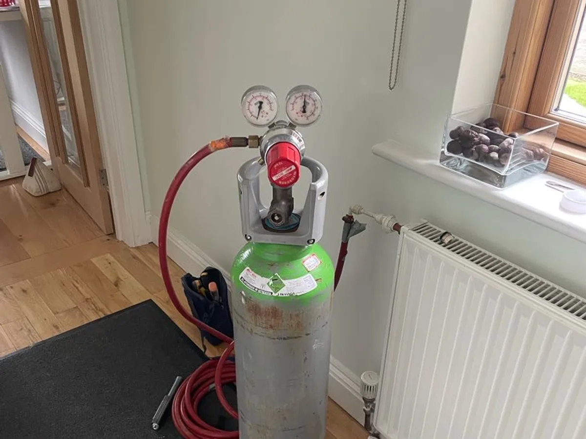 tracer gas cylinder connected to hallway radiator via red hose during leak detection survey