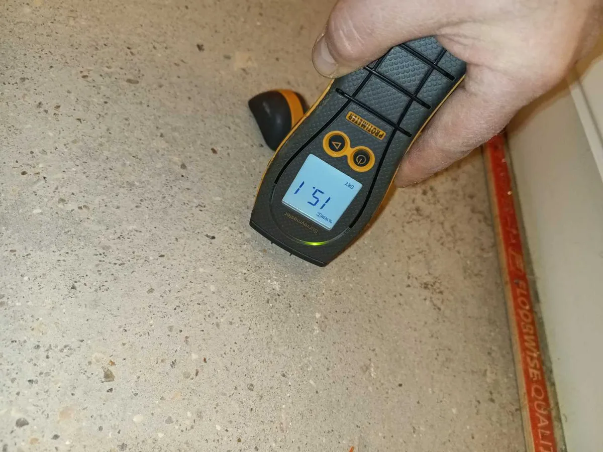 damp meter being held against concrete hallway floor during leak detection investigation