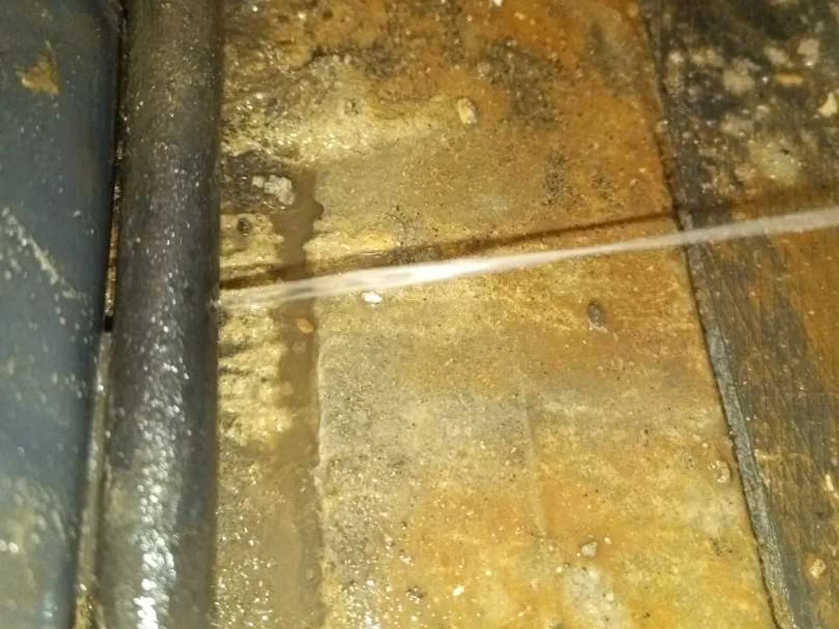 leak found at weeping copper heating pipe with visible water stream in excavated floor channel