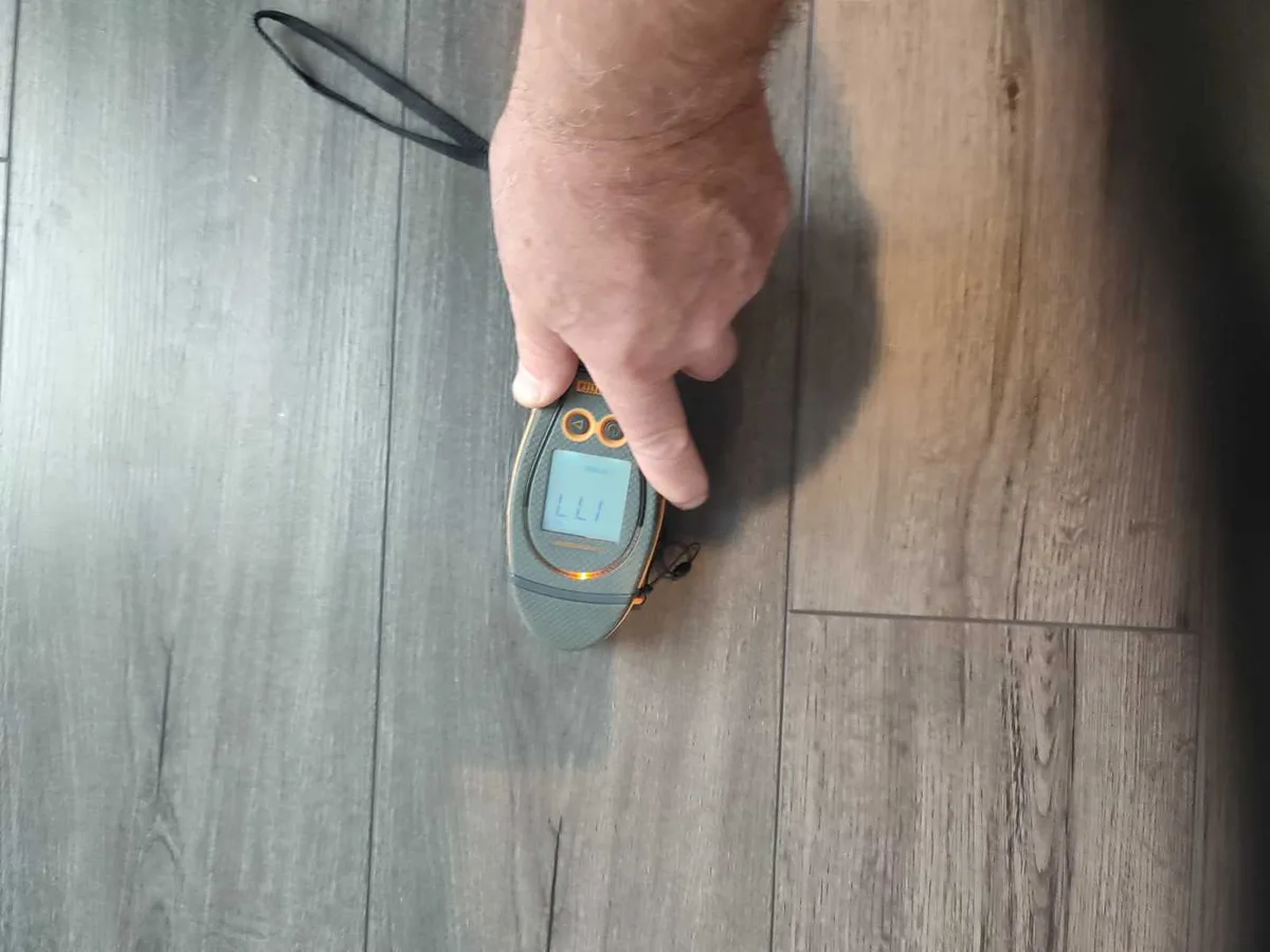moisture meter held against laminate kitchen floor during leak detection survey
