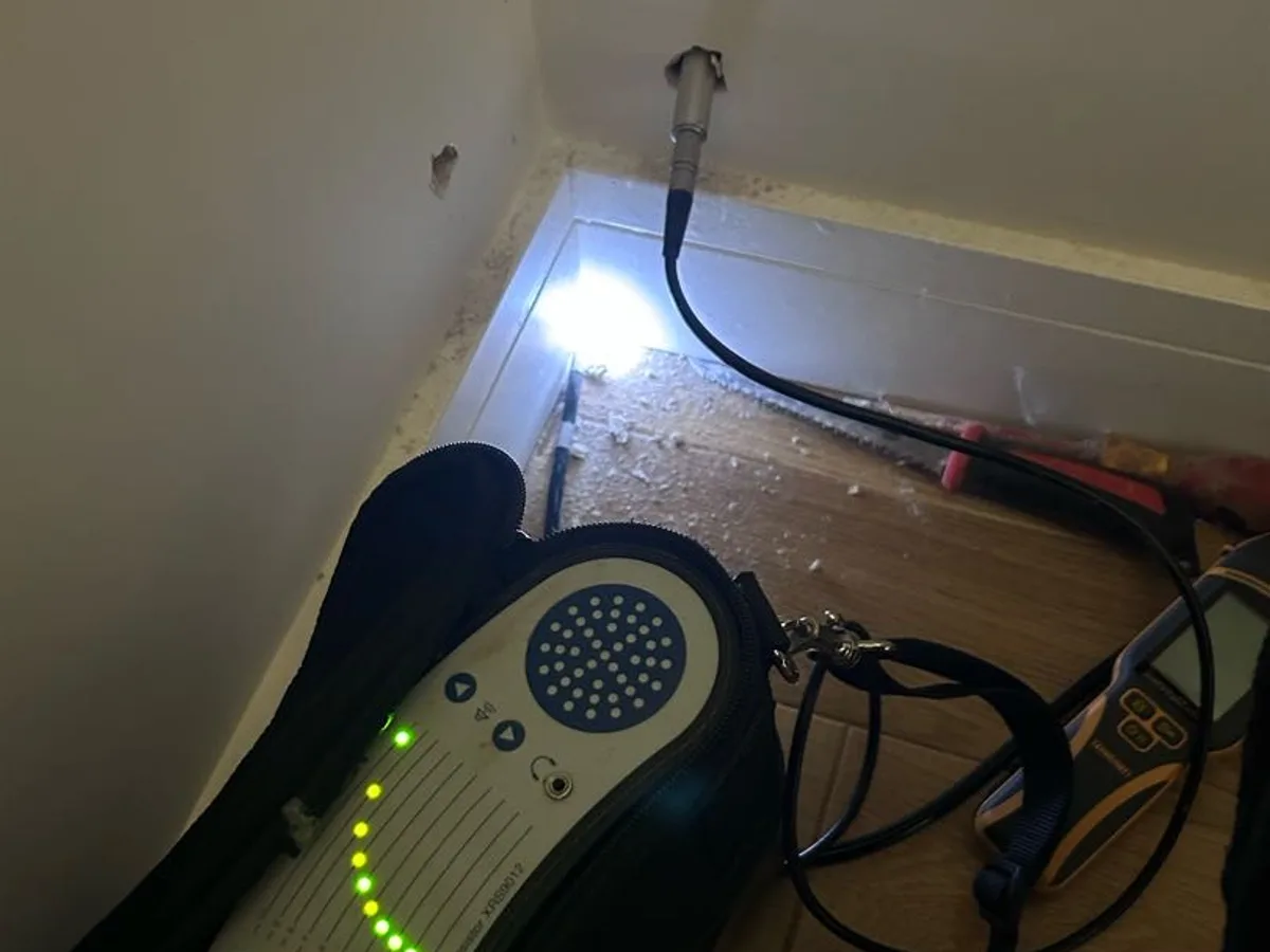 tracer gas detector probe inserted into small hole in plasterboard wall during leak detection