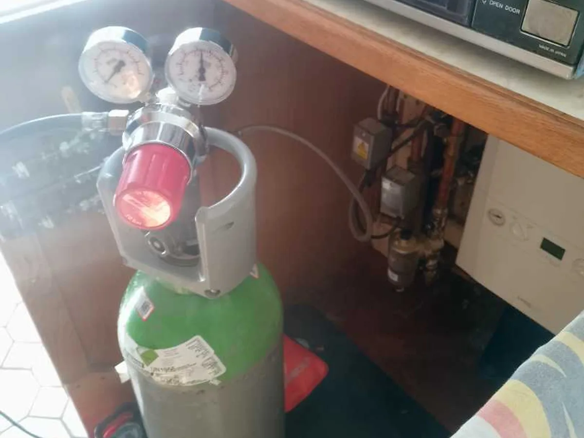 tracer gas cylinder with dual-gauge regulator connected to heating system in boiler cupboard during leak detection