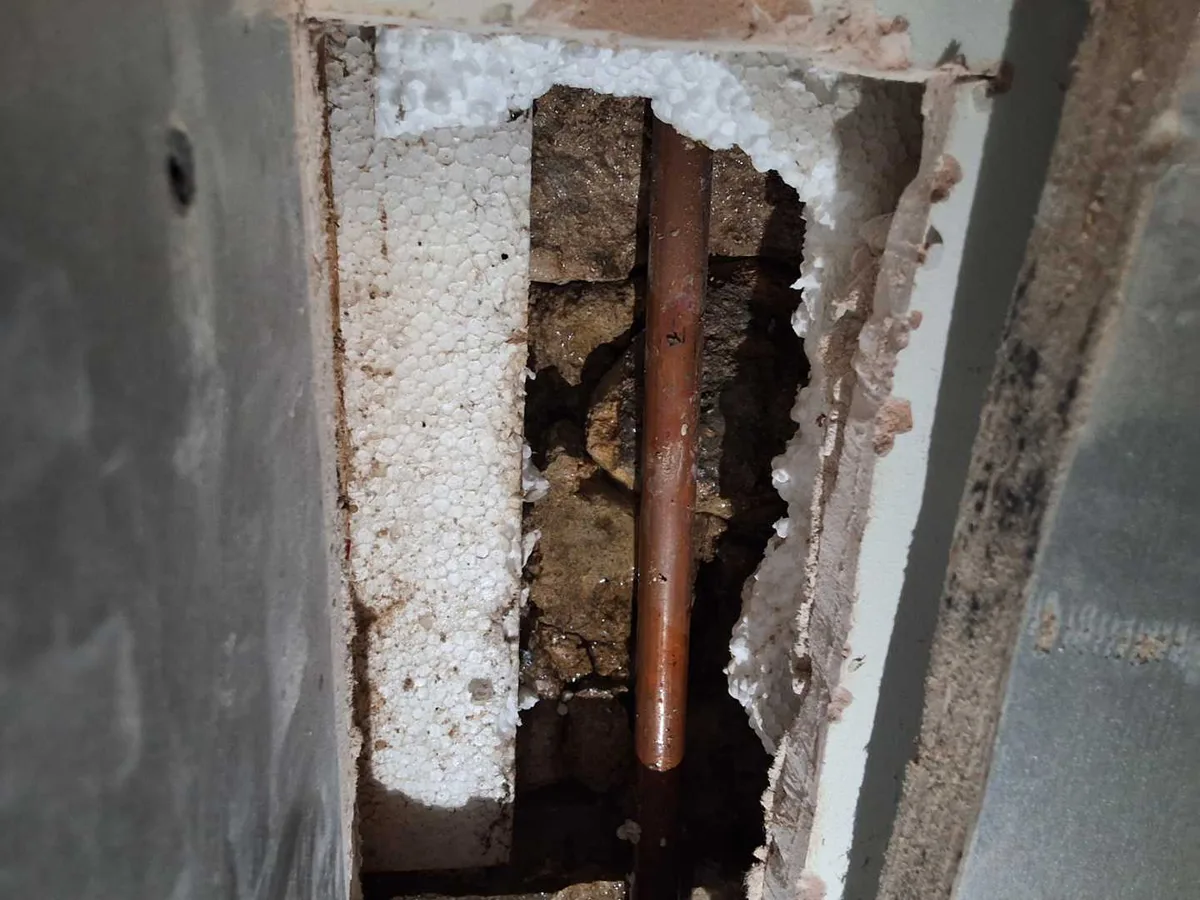 copper heating pipe exposed in wall cavity behind kitchen hob during leak detection