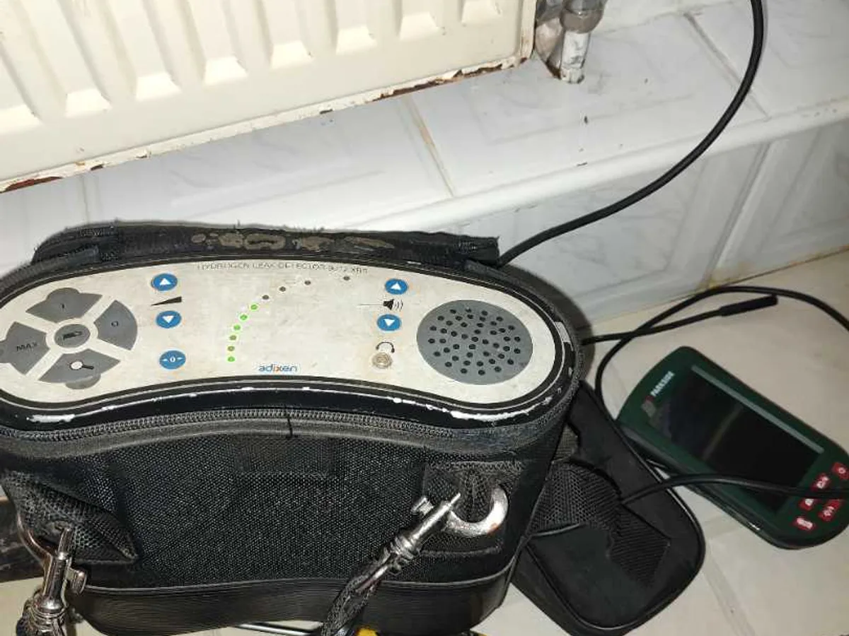 tracer gas detector unit and damp meter laid out in bathroom during leak detection investigation