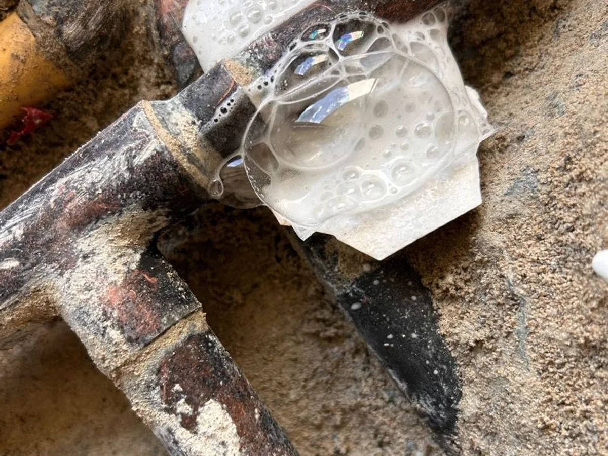 leak located at corroded pipe tee junction beneath hallway screed showing tracer gas bubbles