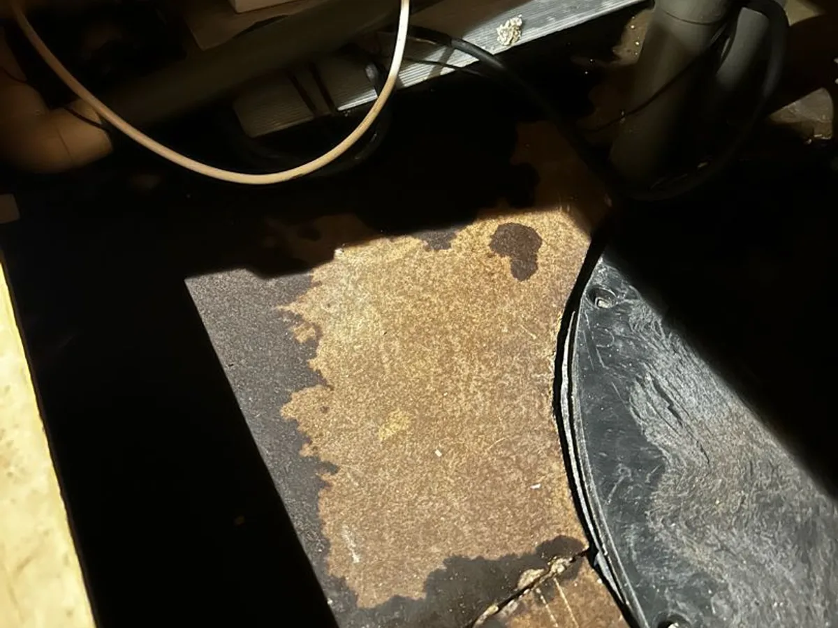 fault exposed at dark water-stained timber subfloor beneath bathroom access panel