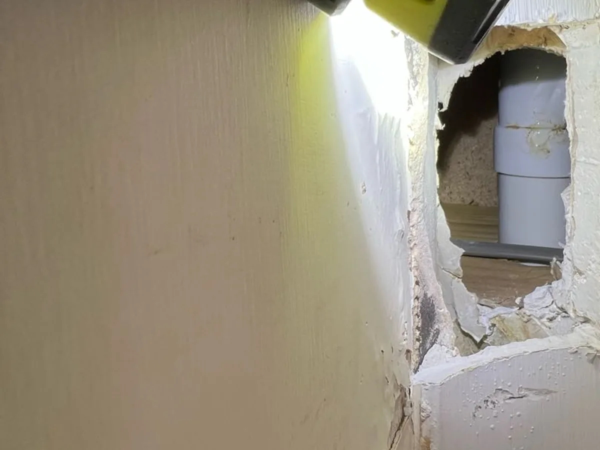 fault identified at waste pipe connection visible through opening in kitchen wall — leak located at