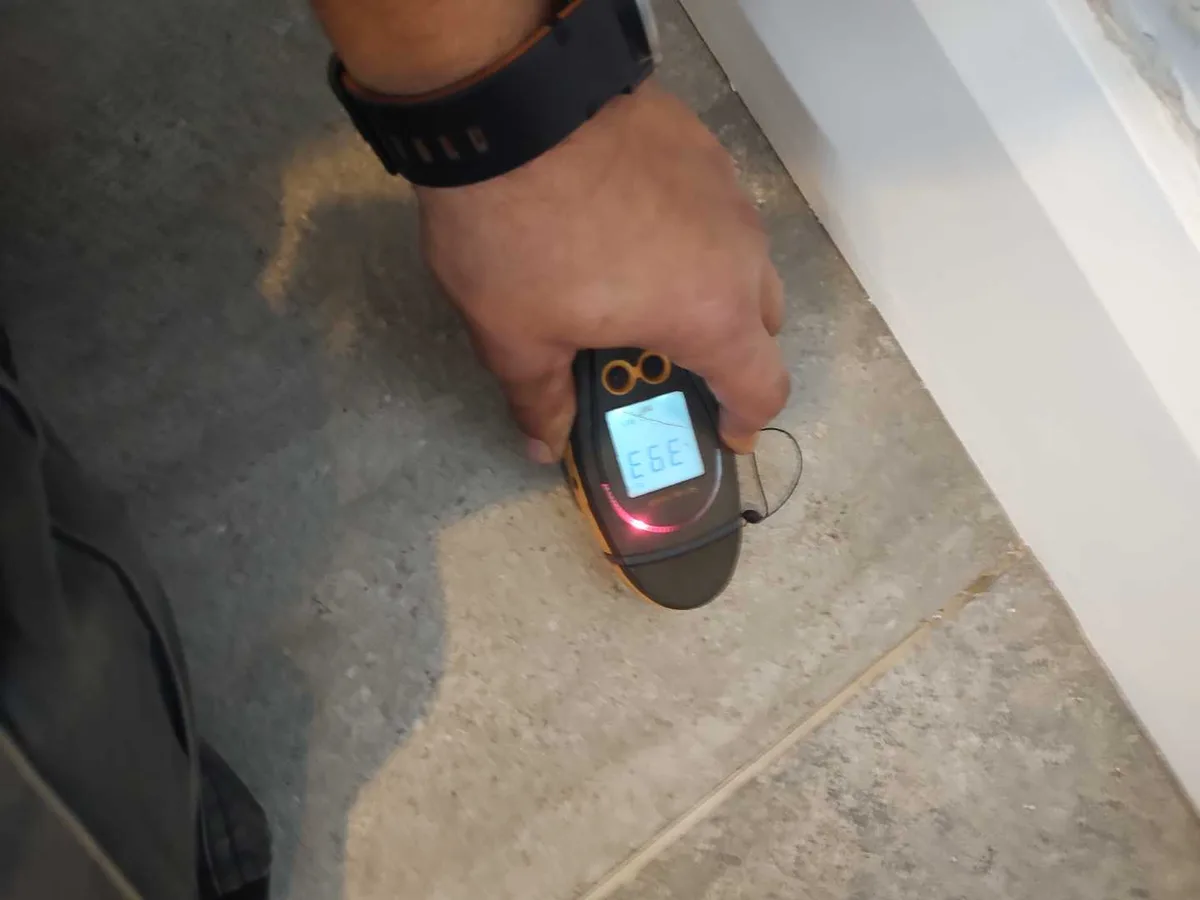 moisture meter held against wet en suite floor tiles during leak detection