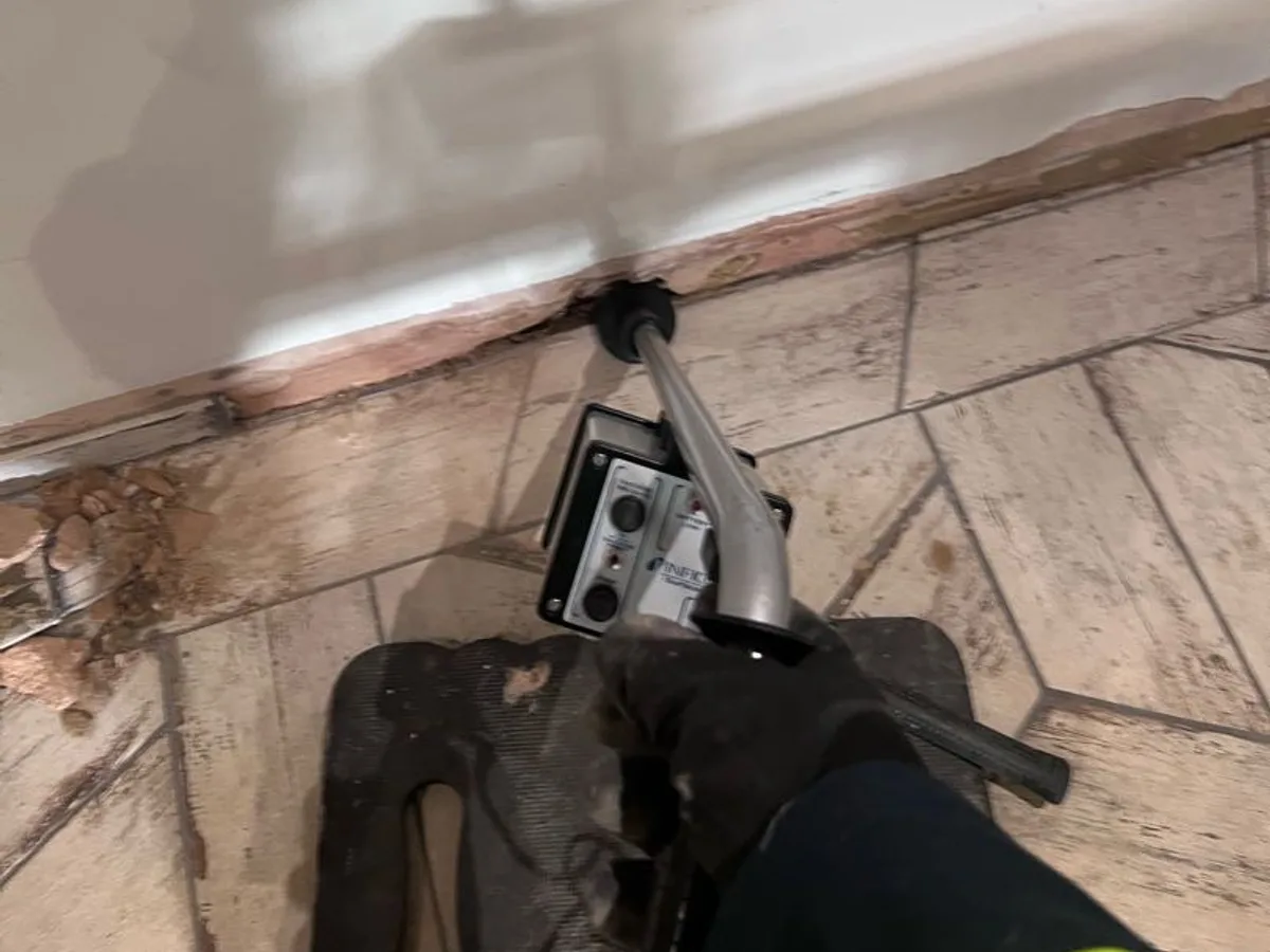 tracer gas detection probe held against kitchen wall skirting during leak detection survey