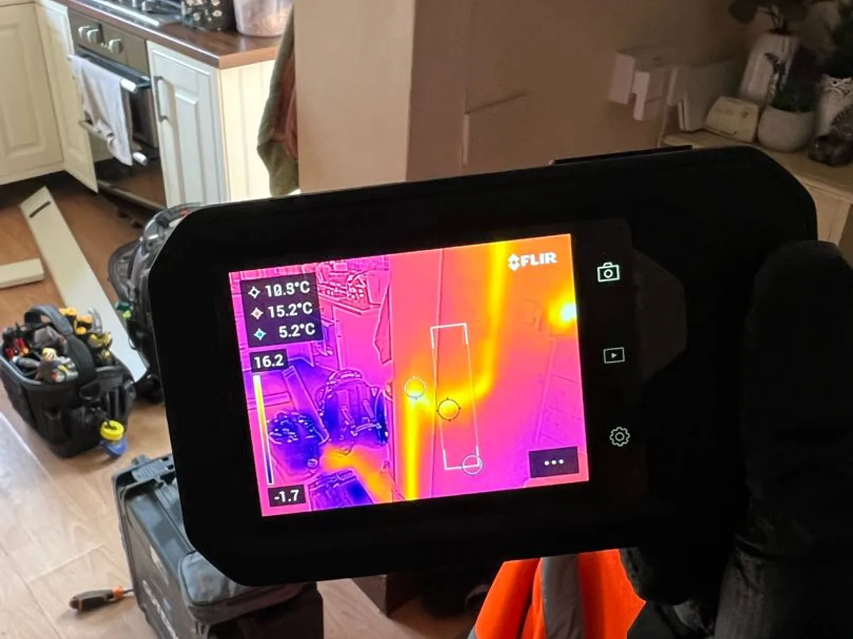 thermal imaging camera screen showing heat signature on kitchen wall during leak detection