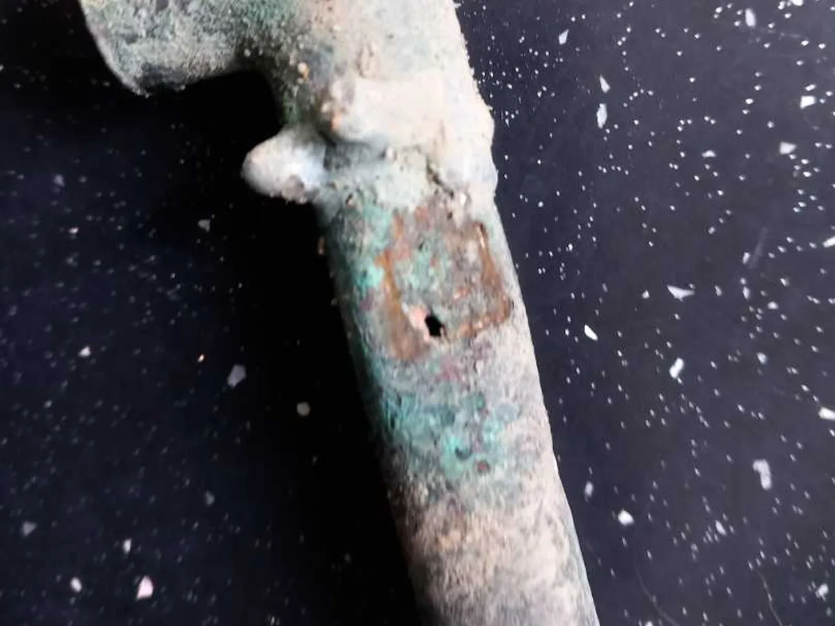 fault identified at heavily corroded copper tee fitting with visible pinhole perforation — leak located at