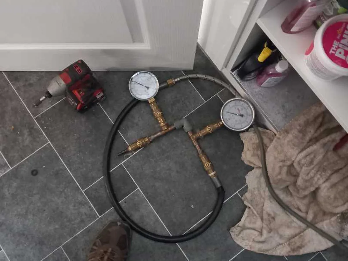 dual pressure test gauges connected to hot-water pipework on kitchen floor during leak detection