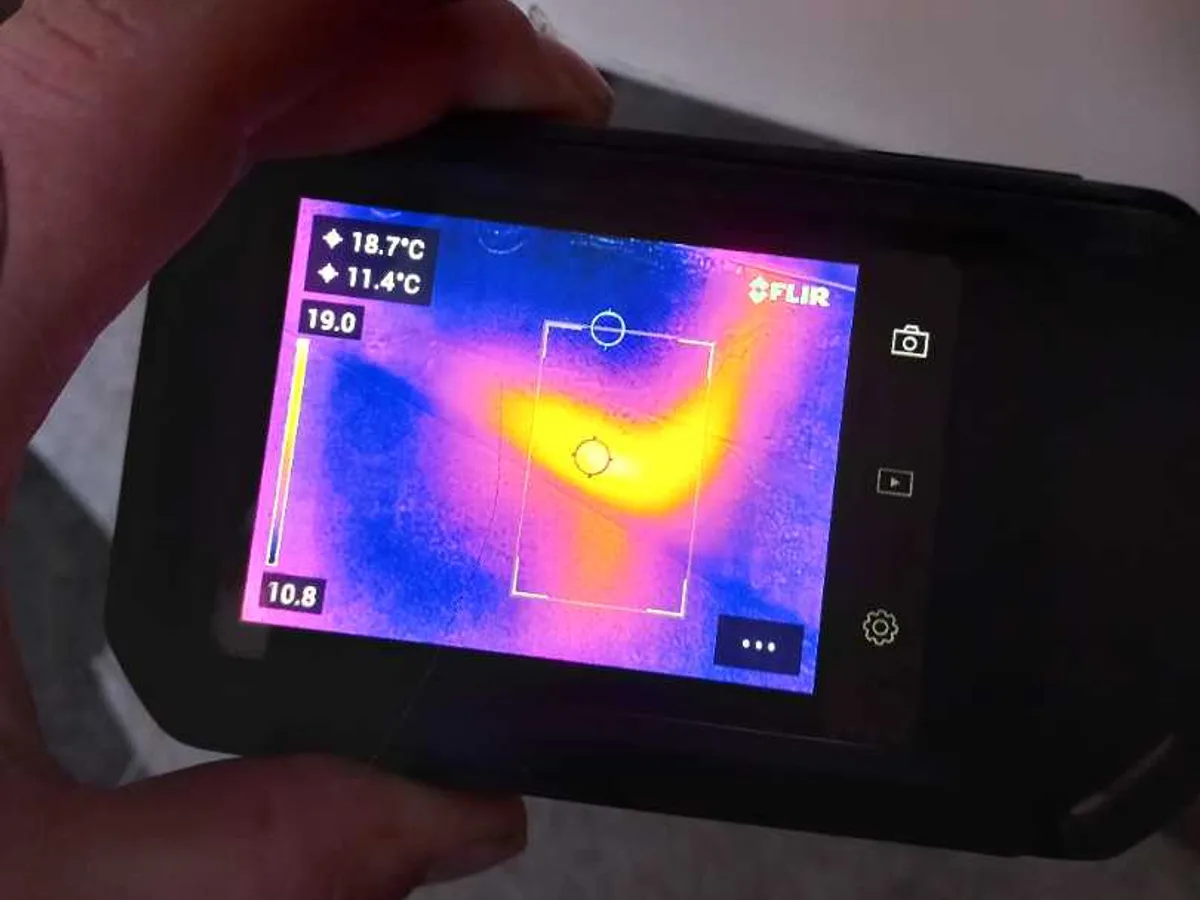handheld thermal imaging camera showing hot-water pipe anomaly in utility room during leak detection