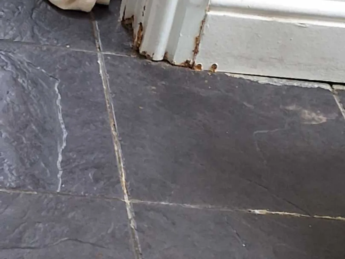 rust-stained and corroded skirting board at floor level showing water damage before works started
