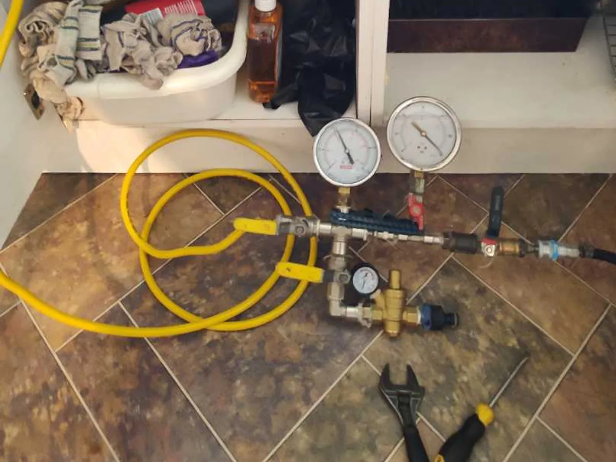 dual pressure gauges connected to hot water feed under kitchen sink during leak detection