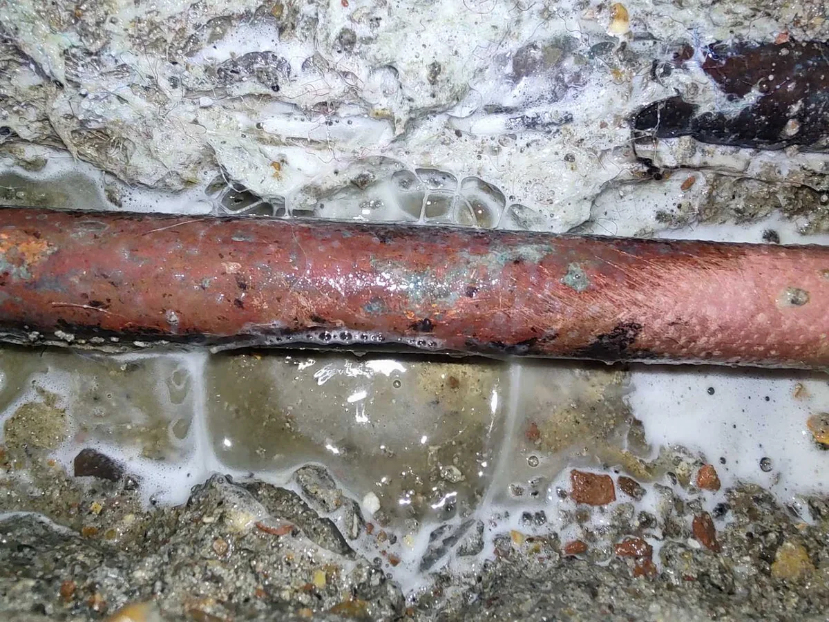 leak located at second fault on heavily corroded copper pipe with water pooling beneath