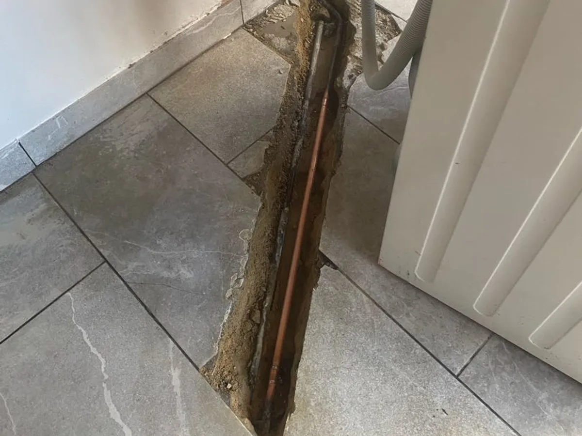 leak exposed at copper pipe in open floor trench beneath washing machine in utility room — leak located at