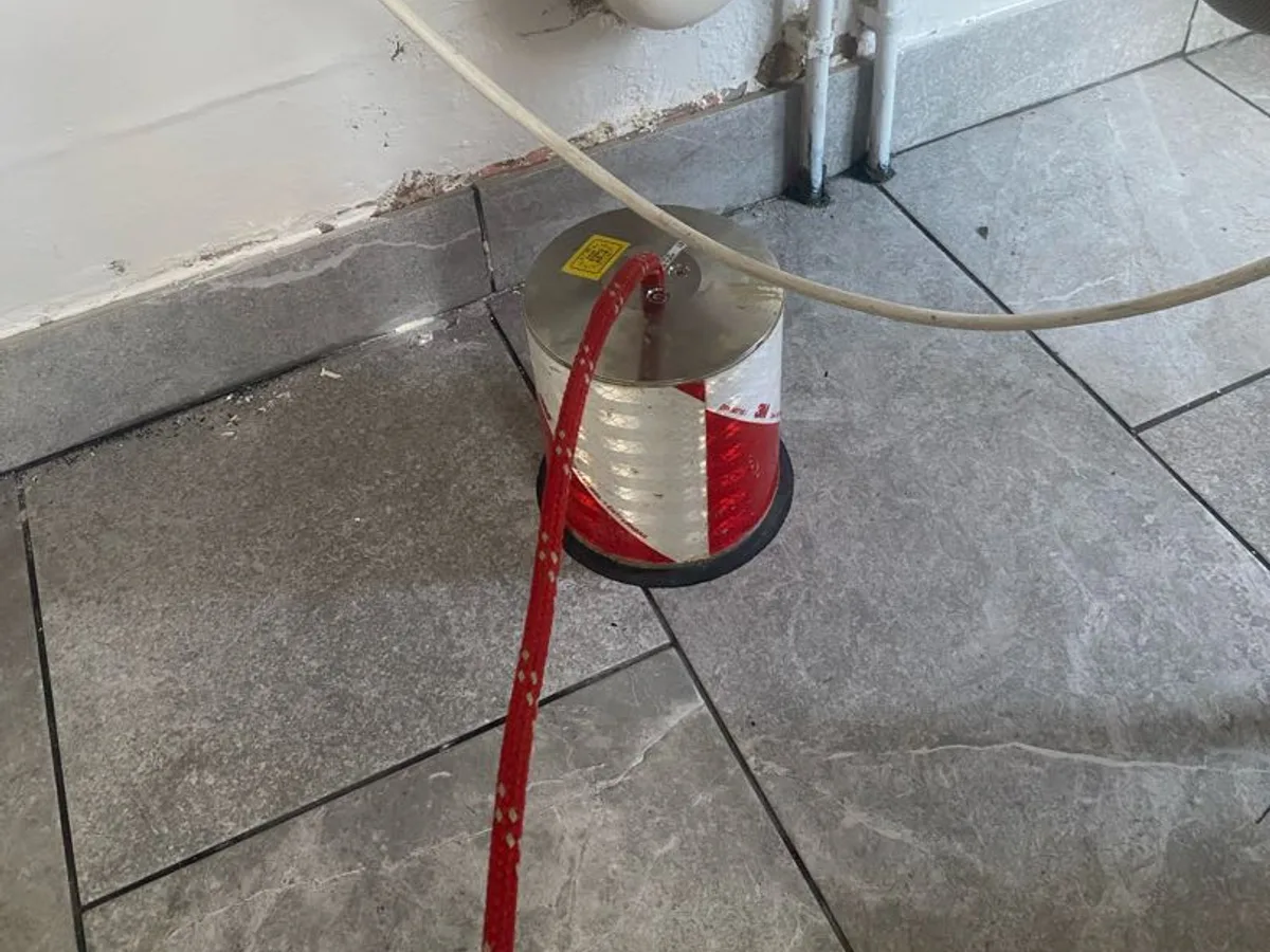 tracer gas canister connected to hot water pipe at utility room floor during leak detection