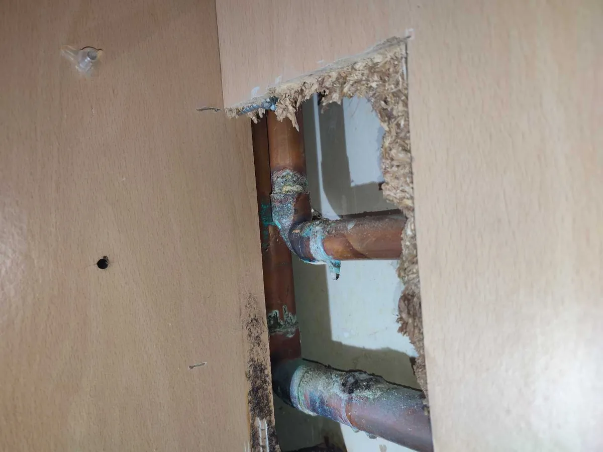 leak located at corroded 22mm copper pipe and elbow joint exposed through cut kitchen cupboard back