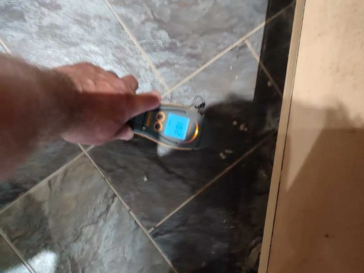 moisture meter held against kitchen floor tiles during leak detection survey