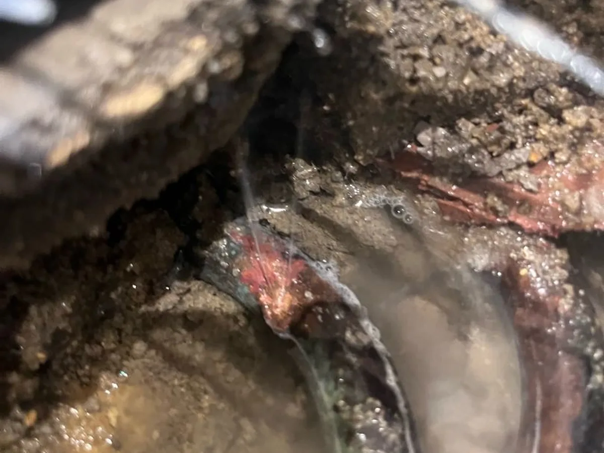 fault exposed at corroded copper hot water pipe embedded in concrete screed beneath kitchen floor