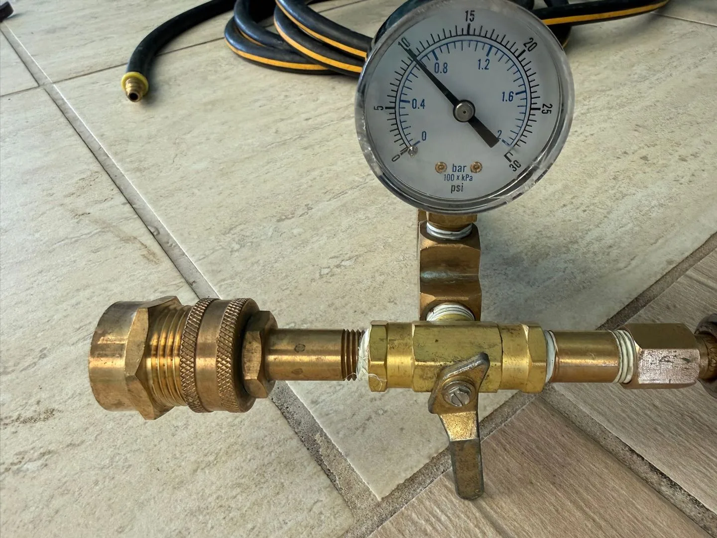 Brass pressure test gauge reading near zero bar with inline ball valve and hose fitting, used during swimming pool leak detection pressure testing.