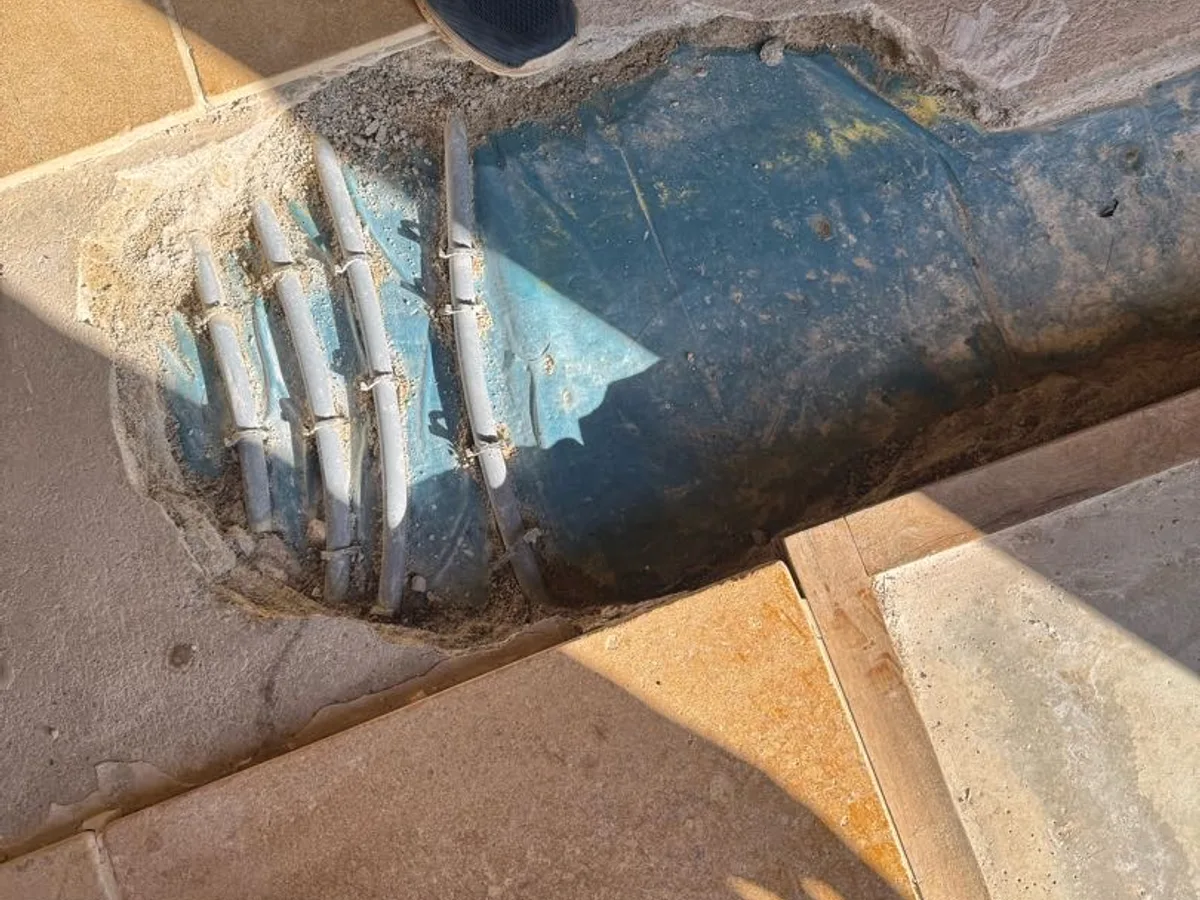 open underfloor pipe channel with visible pipework and membrane being tested during investigation — during leak detection