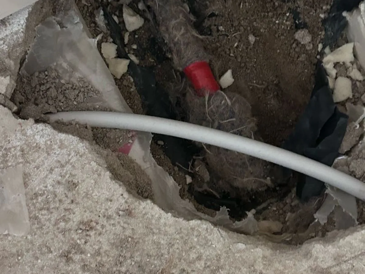 repair in progress at excavated office floor corner showing push-fit coupling on buried pipework