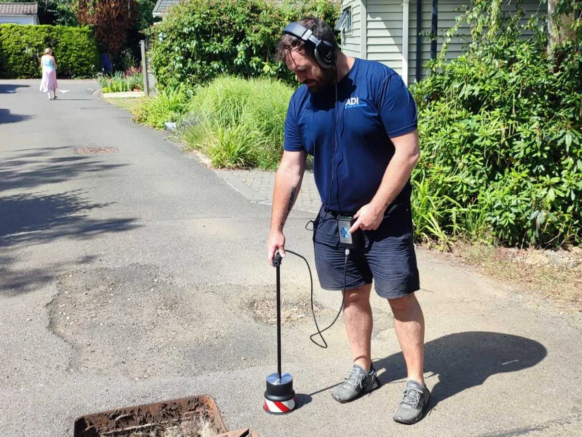 engineer using ground microphone on park road during leak detection