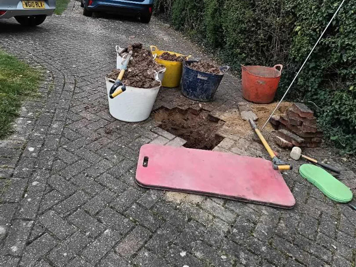 excavated hole in block paving driveway with buckets of spoil where leak was exposed — leak located at
