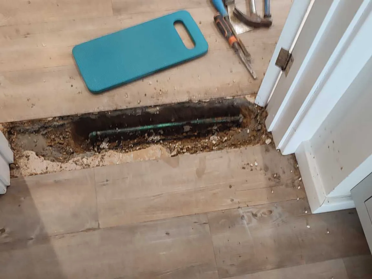 fault exposed at copper pipe embedded in screed beneath excavated vinyl floor tiles