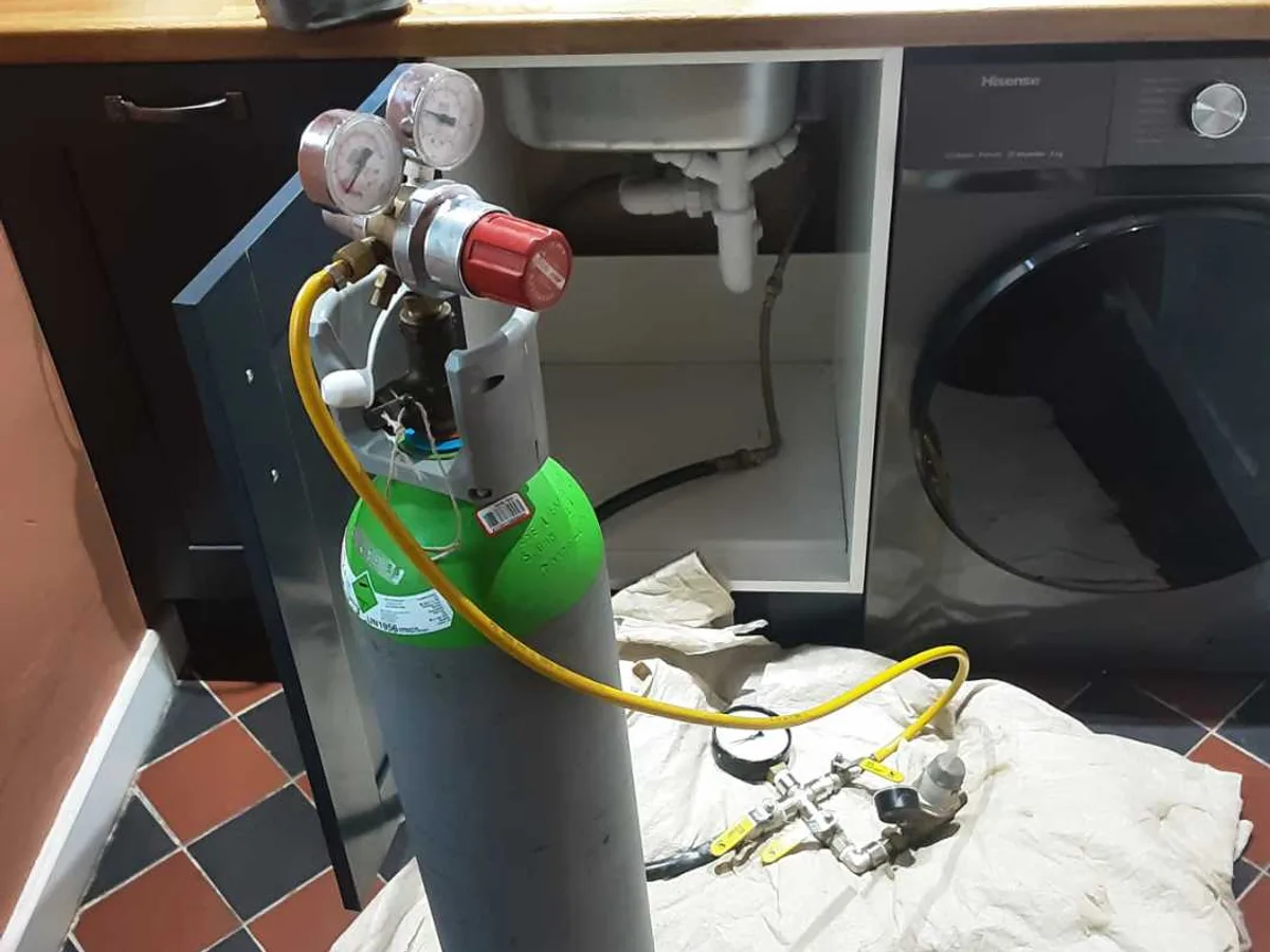 tracer gas cylinder with dual-gauge regulator connected under kitchen sink during leak detection